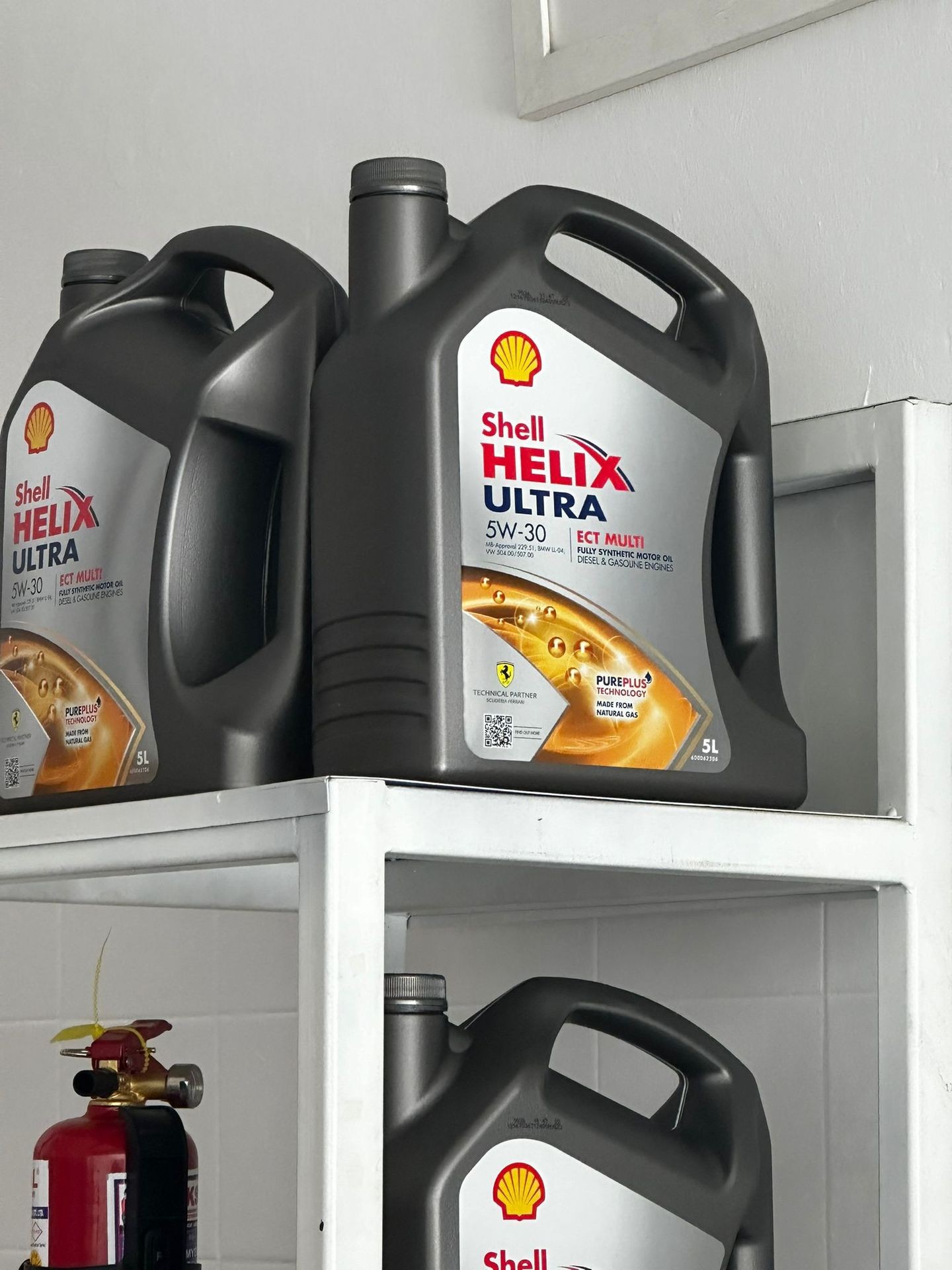 Shell Helix Ultra motor oil containers on a shelf, with a fire extinguisher nearby.