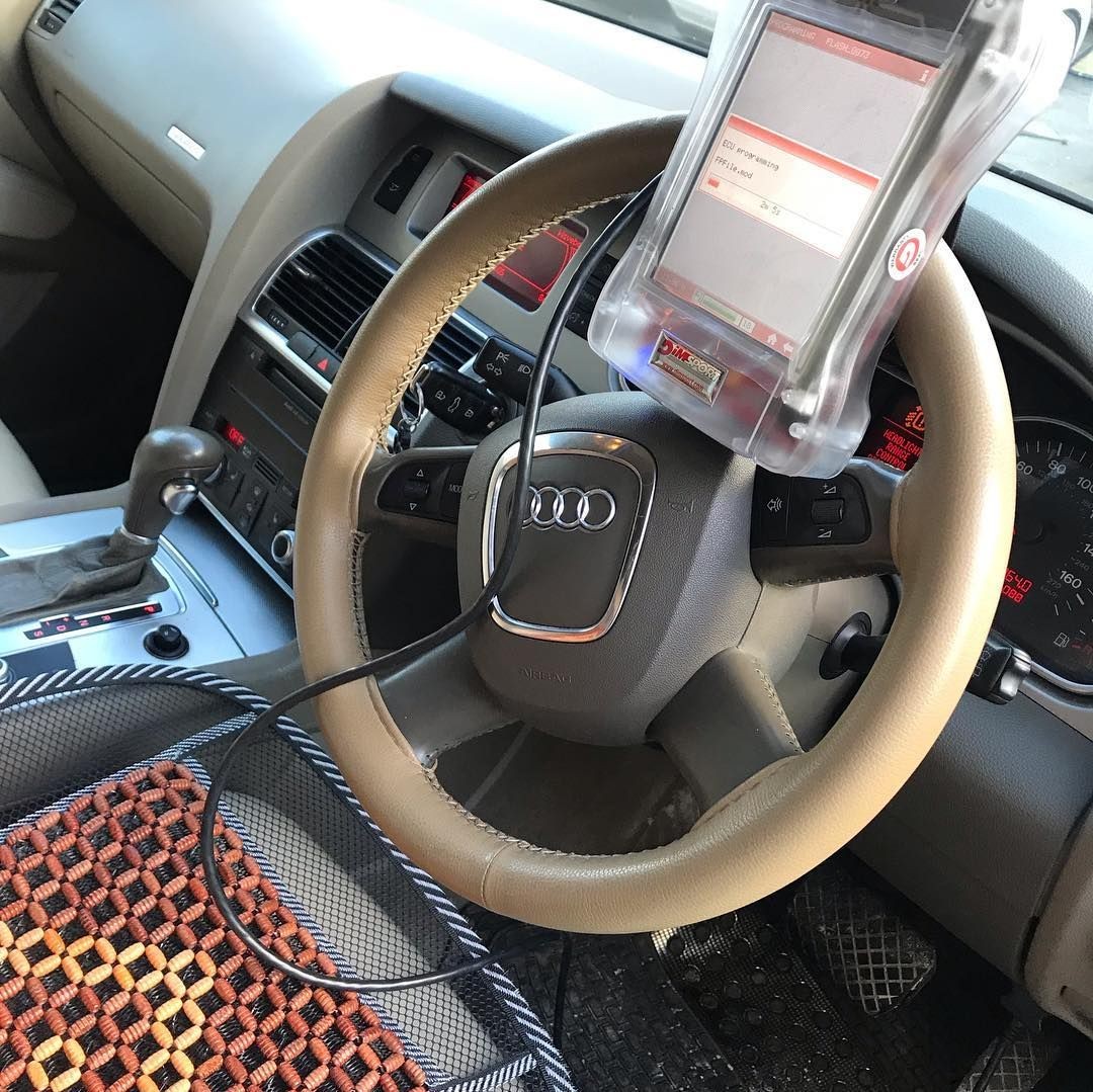 Car interior showing steering wheel with diagnostic device attached, dashboard, and center console.